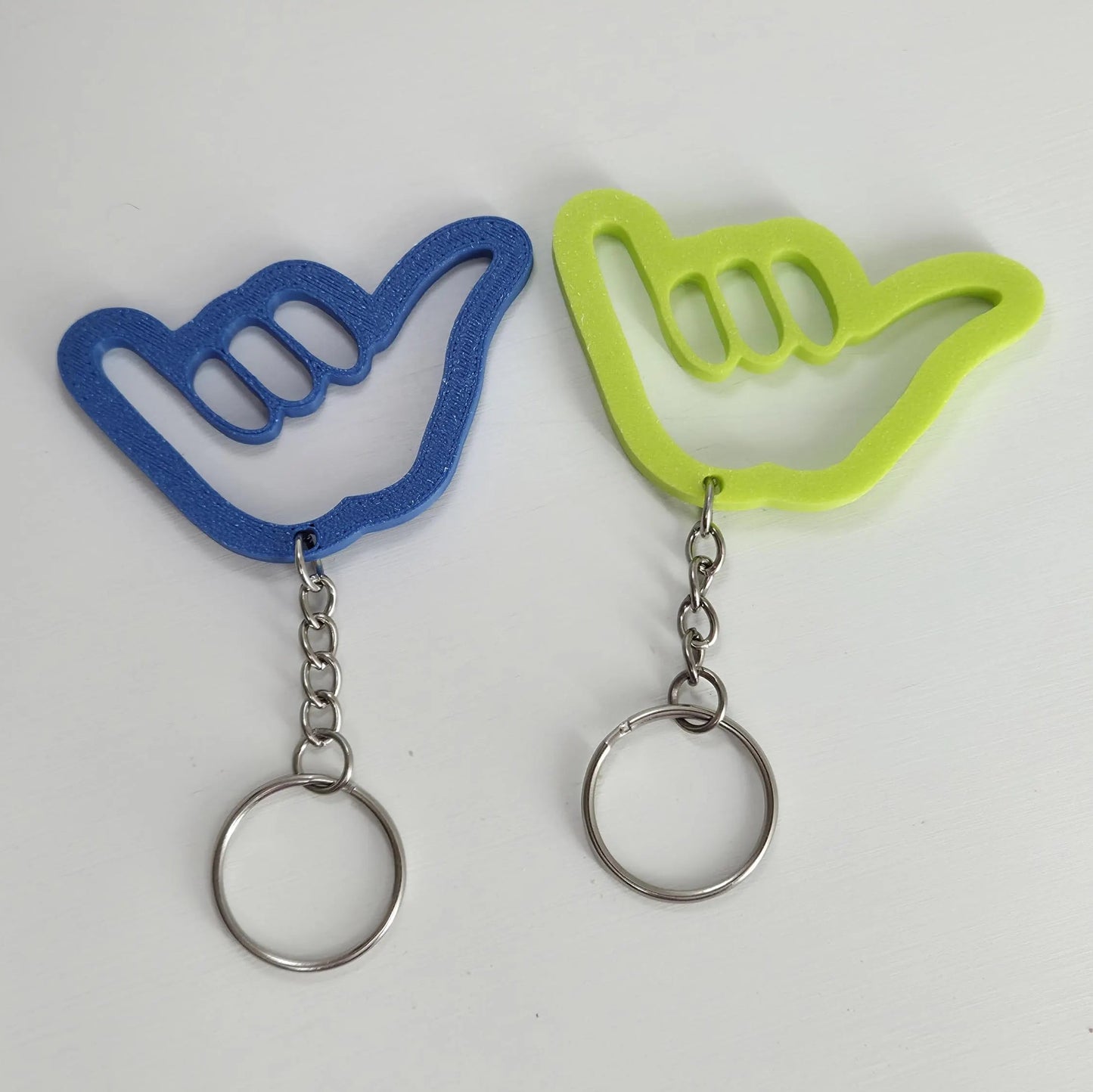 Two keychains shaped like blue and green hand signs on a white background